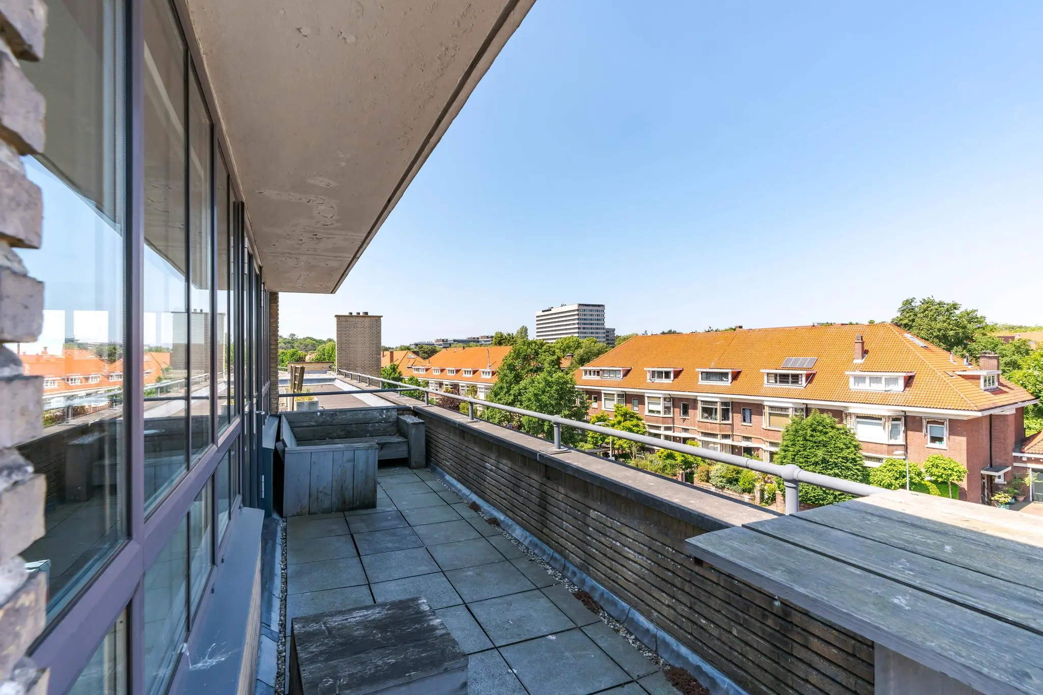Zonnig dakterras met uitzicht op de Van Alkemadelaan en omliggende rode dakpanden in een woonwijk.